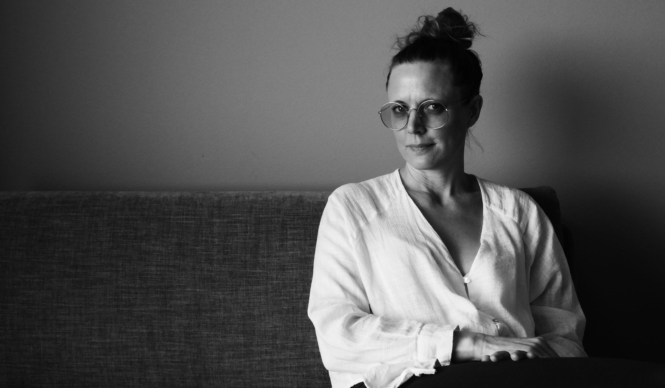 En svartvit bild av Lina Bjarnegård Carlsson som sitter i ena änden av en soffa.