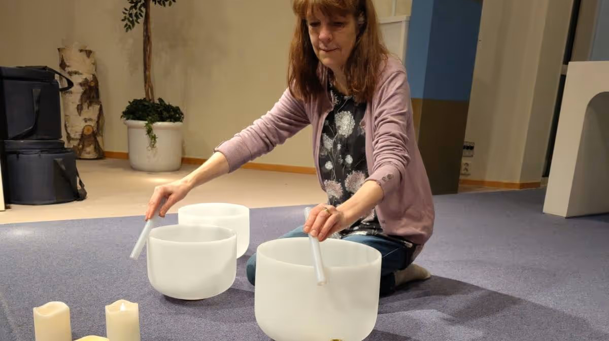 En kvinna sitter på knä på en matta och spelar på mjölkvita glas-skålar.